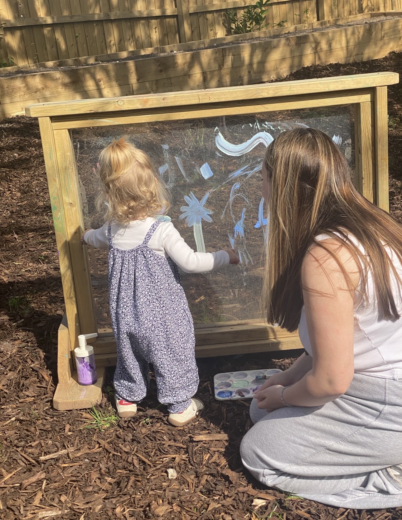 A staff member and child painting together at an outdoor easel