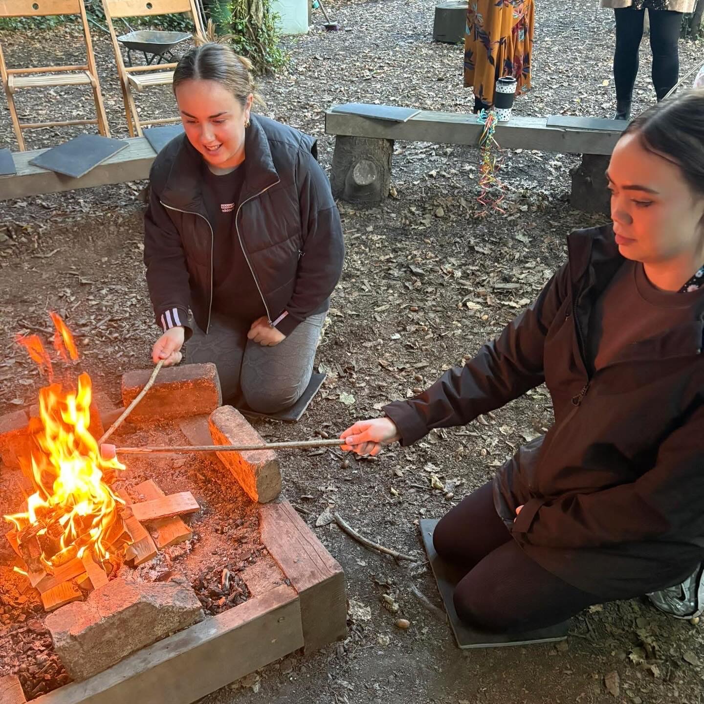 Two forest school leaders tending a fire pit with sticks at Wibli Wobli Newport